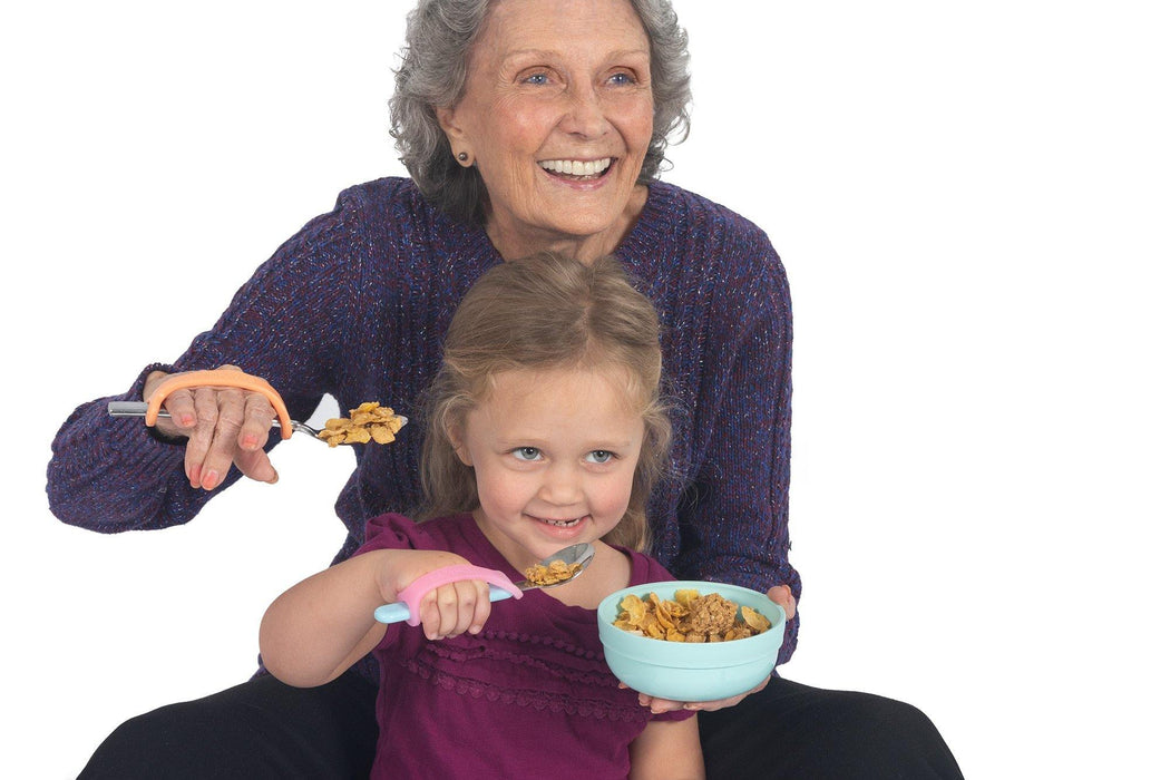 Grandmother and granddaughter eating cereal with spoons with an EaZyHold Grip Aid against a white background
