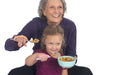Grandmother and granddaughter eating cereal with spoons with an EaZyHold Grip Aid against a white background