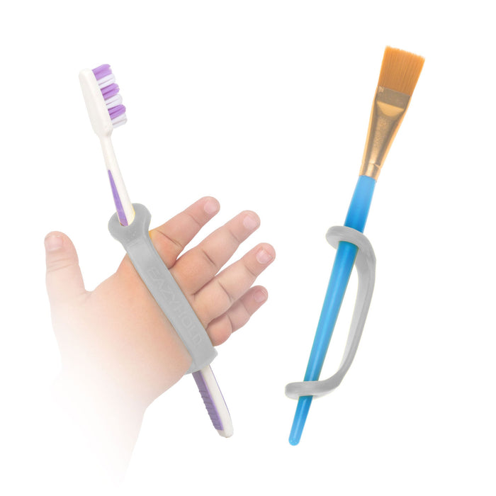 Hand holding a toothbrush with a platinum EaZyHold Grip Aid, next to a paintbrush with a platinum EaZyHold Grip Aid  on a white background