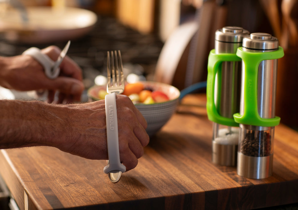 Person holding a fork with an EaZy Hold Grip Aid on a kitchen counter with pepper and salt shakers