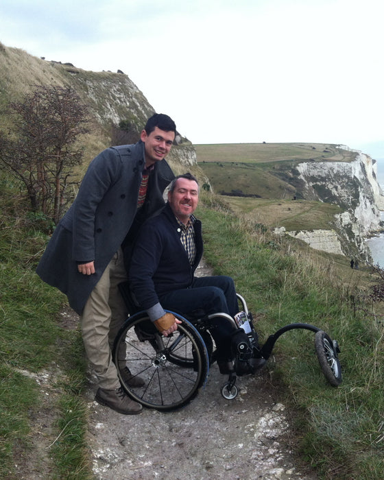 FreeWheel Wheelchair Attachment user with their friend on a rocky path along the cliffside.