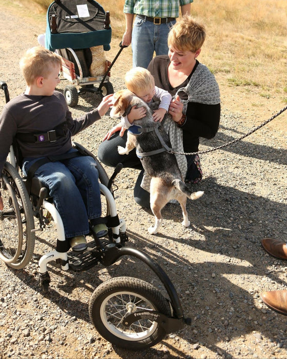 FreeWheel Wheelchair Attachment kid user with their family petting their dog.
