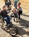 FreeWheel Wheelchair Attachment kid user with their family petting their dog.