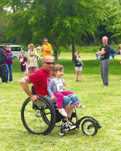 FreeWheel Wheelchair Attachment user pushing their kid on grass.