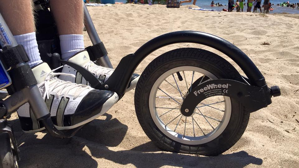 Detail of a FreeWheel Wheelchair Attachment Black on a wheelchair on the beach.