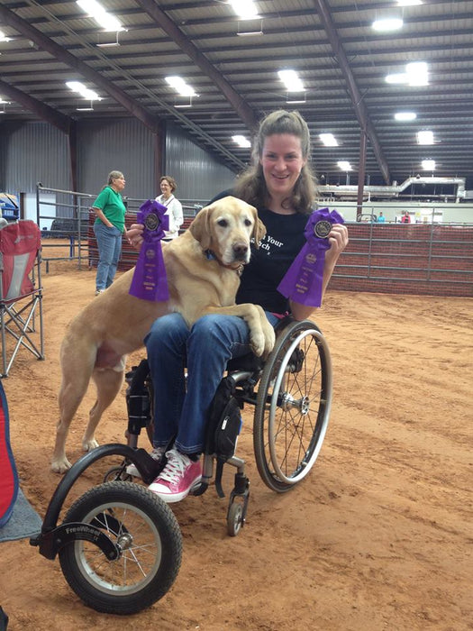 FreeWheel Wheelchair Attachment user in a dog event on dirt with their dog resting on their lap.
