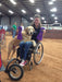 FreeWheel Wheelchair Attachment user in a dog event on dirt with their dog resting on their lap.