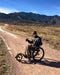 FreeWheel Wheelchair Attachment user on a dirt path with mountains in the background.