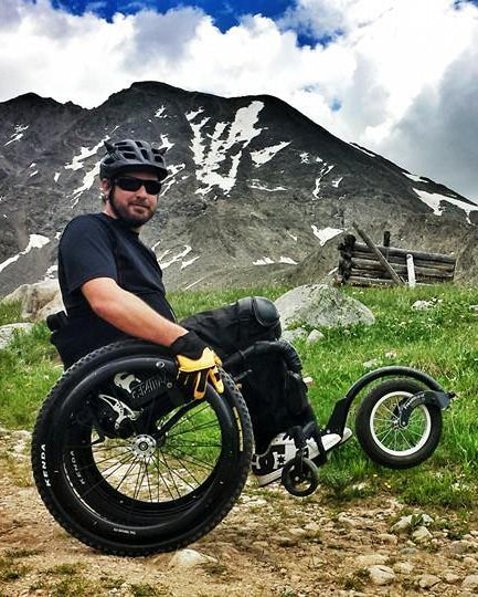 FreeWheel Wheelchair Attachment user popping a wheelie with a mountain in the background.