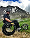 FreeWheel Wheelchair Attachment user popping a wheelie with a mountain in the background.