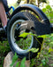 Detail of a FreeWheel Wheelchair Attachment Black on a wheelchair outdoors going over a rock.