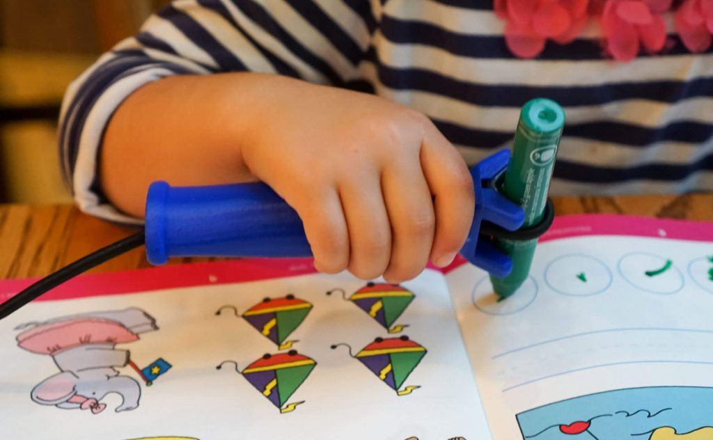 Kid's hand holding the functionalhand Universal Cuff Grip Aid with a marker being held to use a coloring book with cartoon characters.