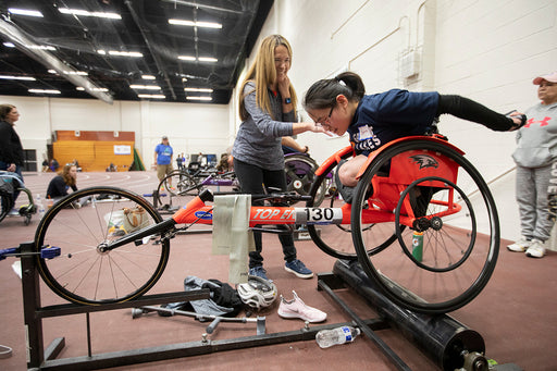 GLASA athletes in a row using a roller with a racing wheelchair with a coach helping them with technique.