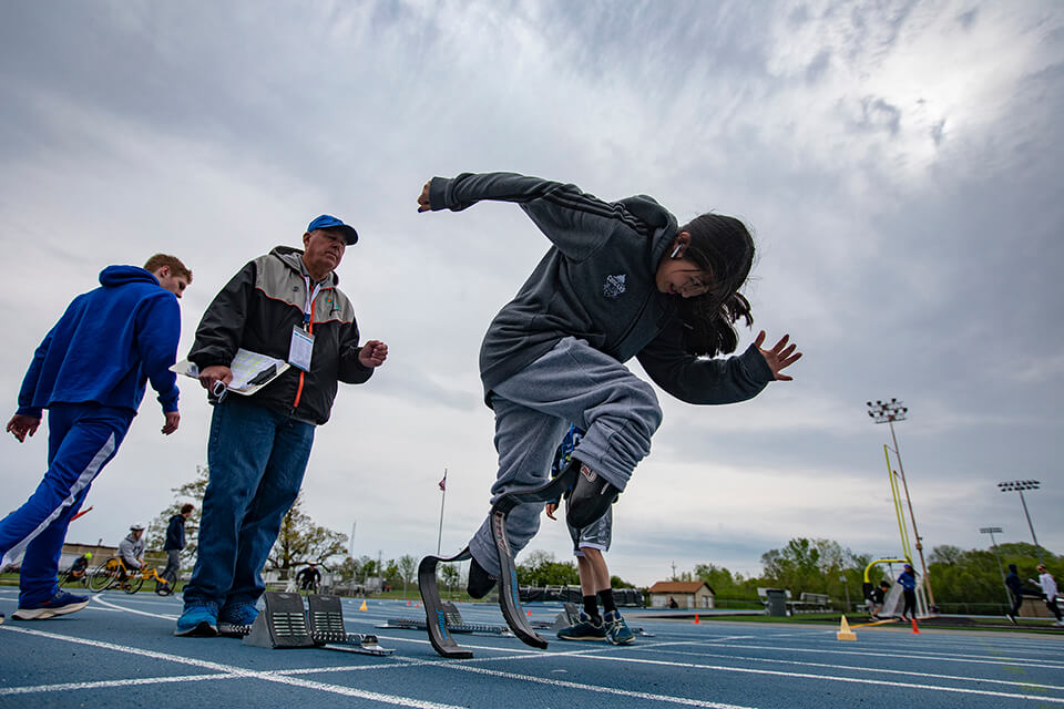 GLASA athlete with double below knee amputations getting out of the starting blocks on the track while their coach watches.