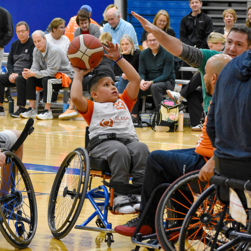 GLASA Wheelchair basketball game on an indoor court with a kid getting ready to shoot the basketball and an adult attempts to block them 