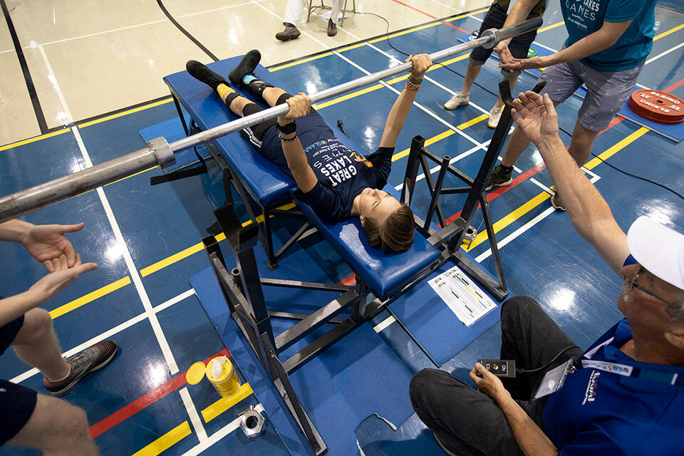 Athlete bench pressing with spotters at the ends of the barbell at the Great Lakes Games.
