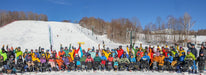Group of Green Mountain Adaptive Sports participants in colorful winter clothing on a snowy slope with ski lifts and trees in the background