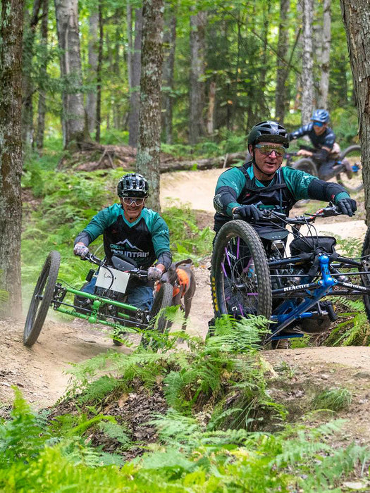 Three individuals from Green Mountain Adaptive Sports on adaptive mountain bikes navigating a forest trail