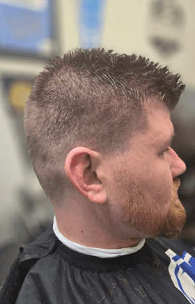 Man with a styled haircut and beard, wearing a black barber cape