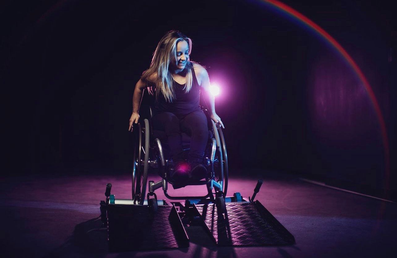 Person in a wheelchair using an Invictus Active Wheelchair trainer indoors.
