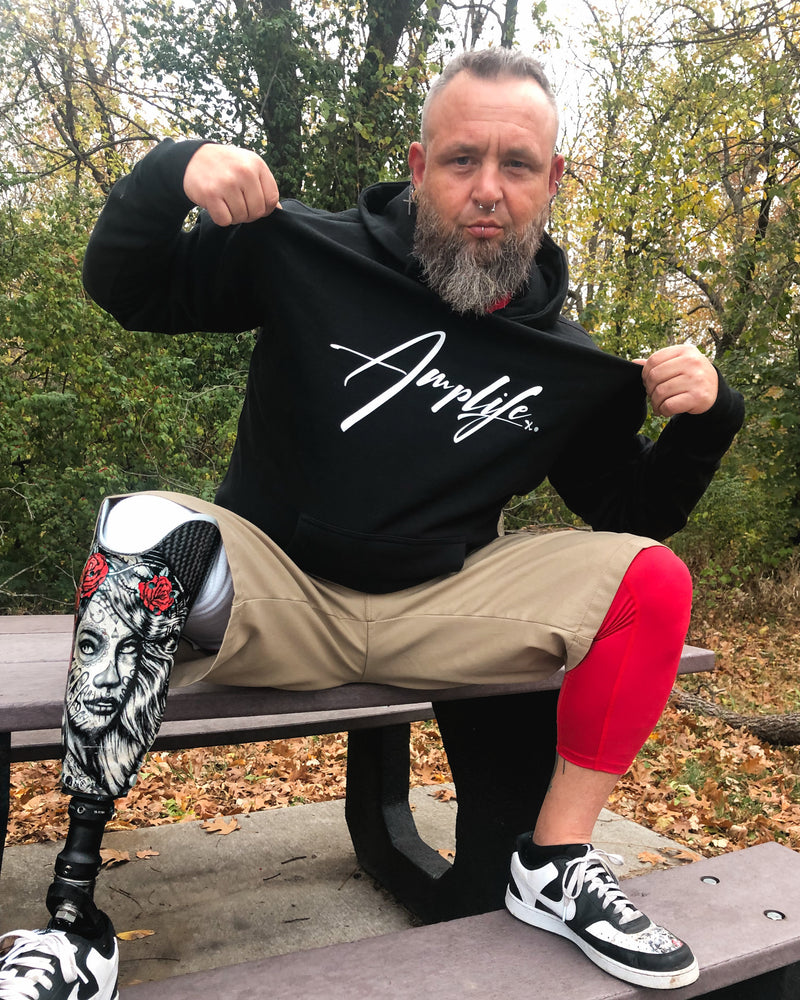 Jason Loftiss rockin’ his Amplife® while wearing the Amplife® Signature Hoodie sitting on a table in the woods while showing the design.