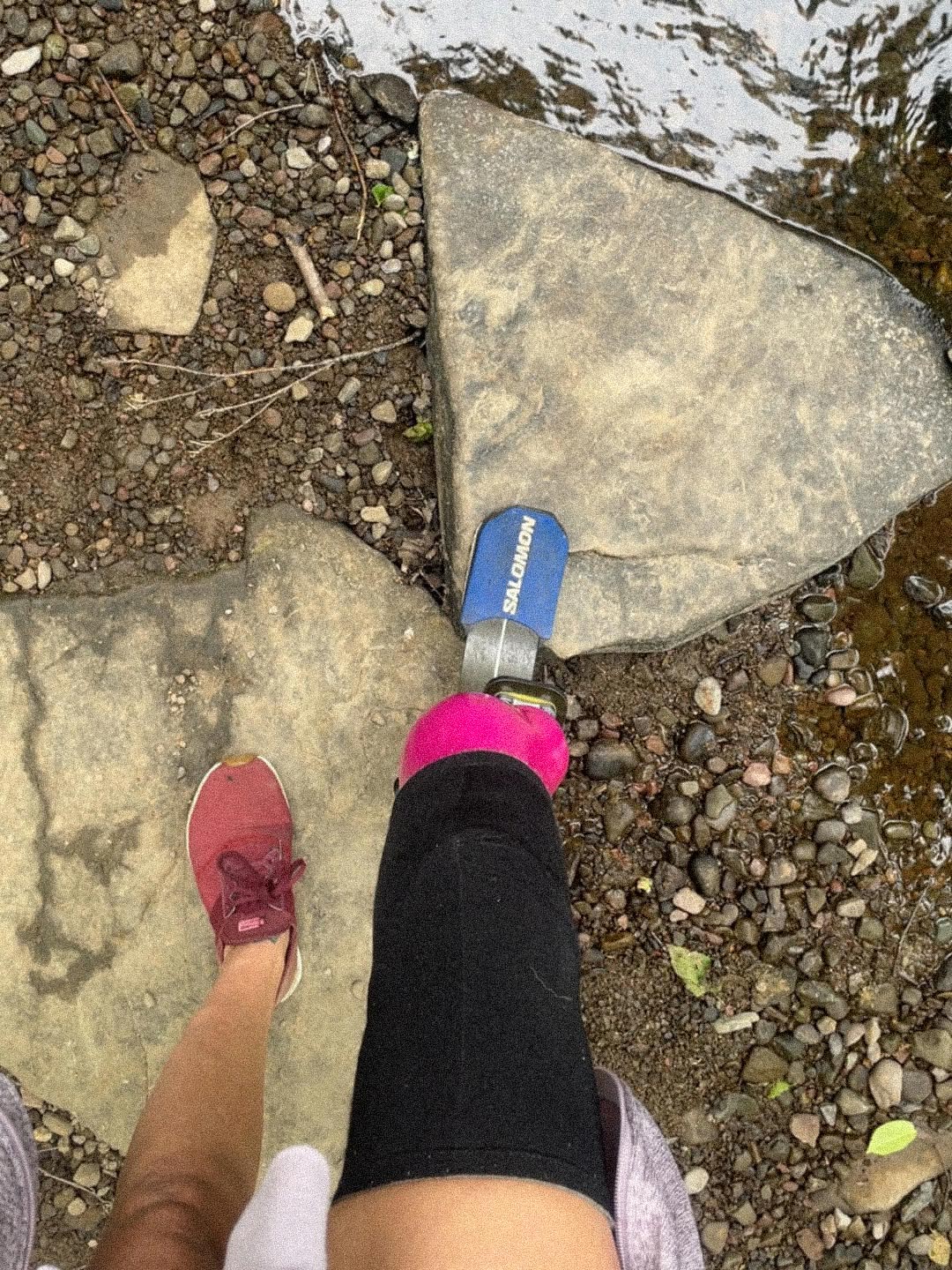 Team Amplife® Ambassador Jenny Morgan stepping onto a rock with her prosthetic leg on a rocky and wet ground