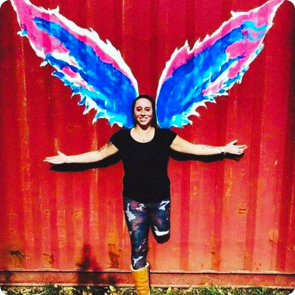 Portrait of Team Amplife® Ambassadors Kara Wolter standing in front of colorful angel wings against a red wall