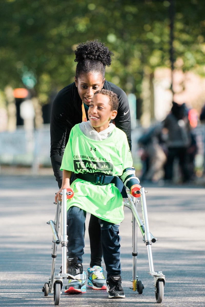 Woman helping a child from Kennedy Krieger Institute with crutches in an outdoor setting
