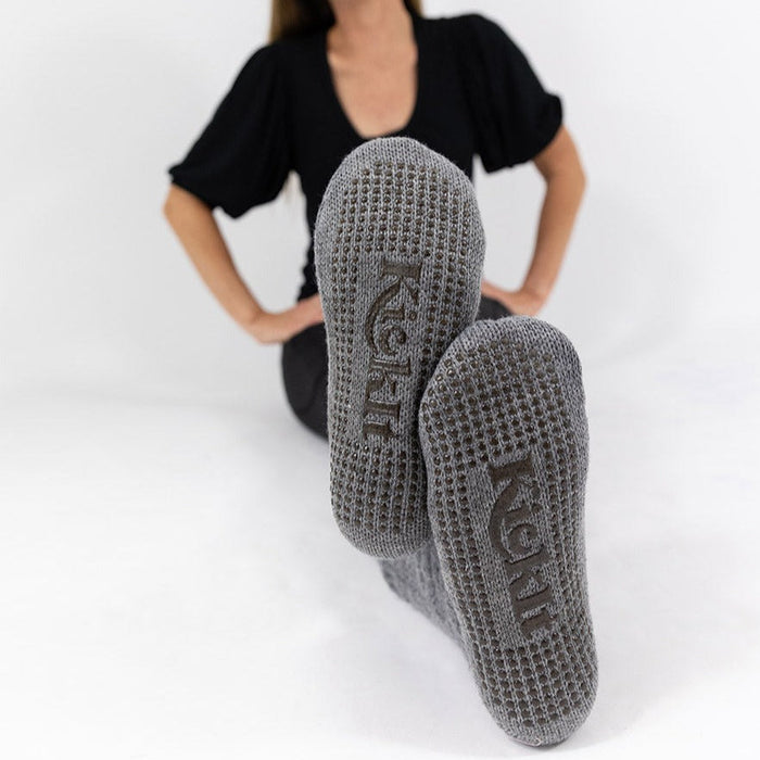 Detail of person sitting on ground with the KickIt Hospital Slipper Socks soles being shown on a white background