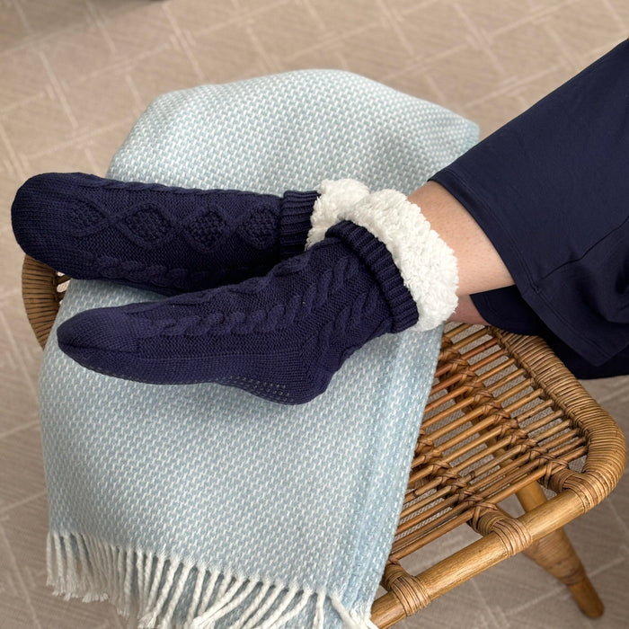 Person resting their legs on a wooden bench on light blue blanket while wearing the KickIt Navy Blue Hospital Slipper Socks on a white background
