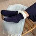 Person resting their legs on a wooden bench on light blue blanket while wearing the KickIt Navy Blue Hospital Slipper Socks on a white background