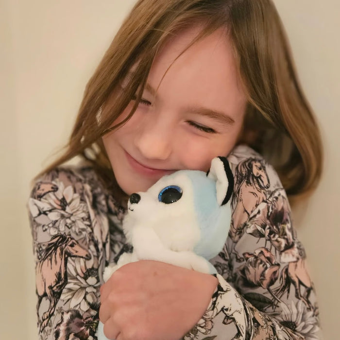 Child holding a white plush toy with blue eyes against a plain background