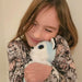 Child holding a white plush toy with blue eyes against a plain background