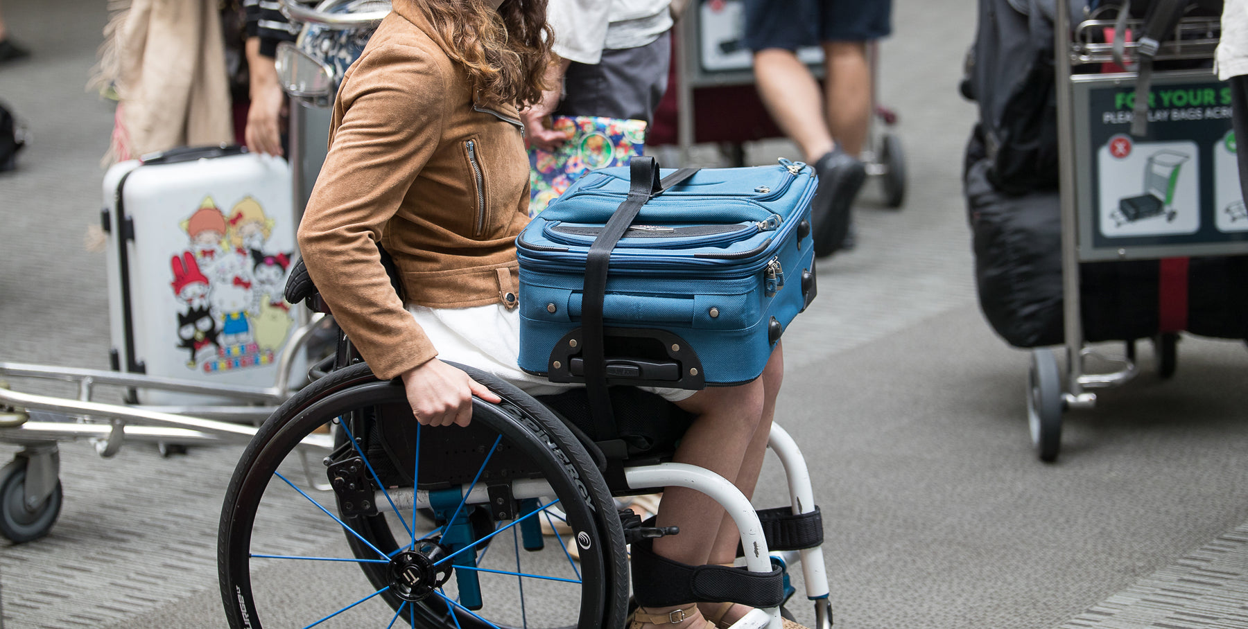 Person navigating through the airport while their suitcase rests on their lap in their wheelchair using the Adaptdefy Lapstacker