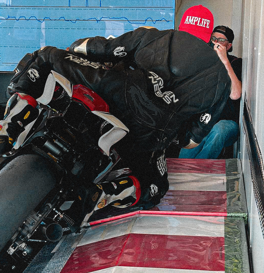 Team Amplife® Ambassador Michael Braxton Jr. wearing the Amplife® Curved Bill Snapback while riding a motorcycle simulator