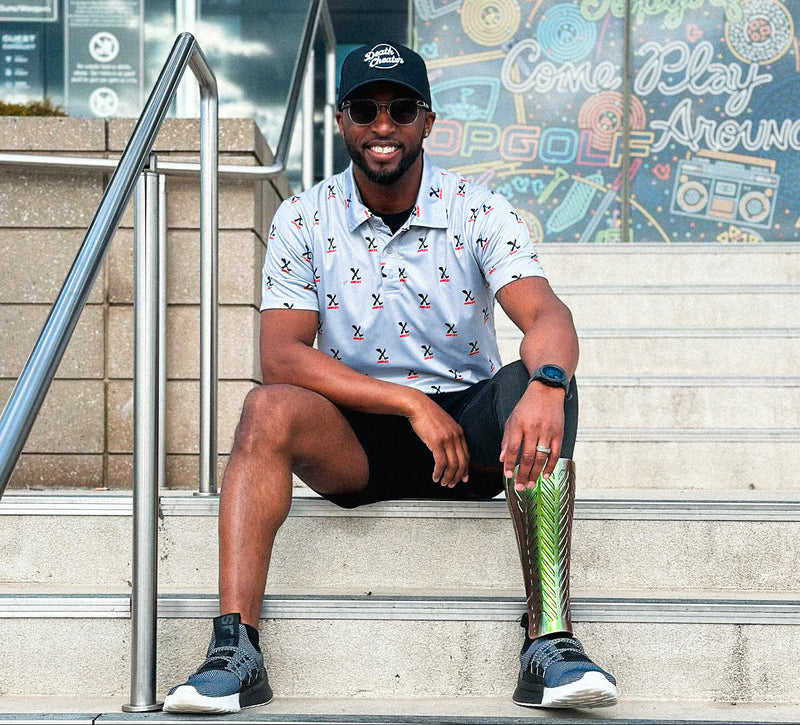 Team Amplife® Ambassador Michael Braxton Jr. wearing the Amplife® Allover Polo and Death Cheater® Halo Curved Bill Snapback on the steps of a Top Golf