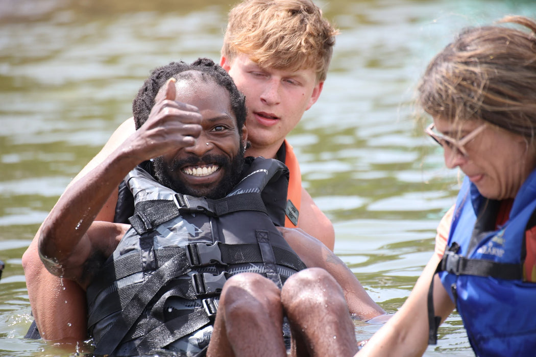 MAS Day at the Lake adaptive water ski participant smiling and giving a thumbs up while being assisted by a volunteers at Smithville Lake