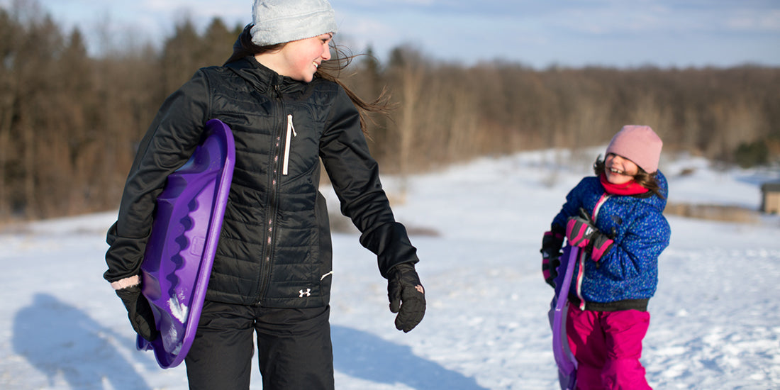 Two people in winter clothing walking on a snow-covered field with trees in the background. The jackets feature a MagZip Magnetic Zipper Top Stopped Round Base #5