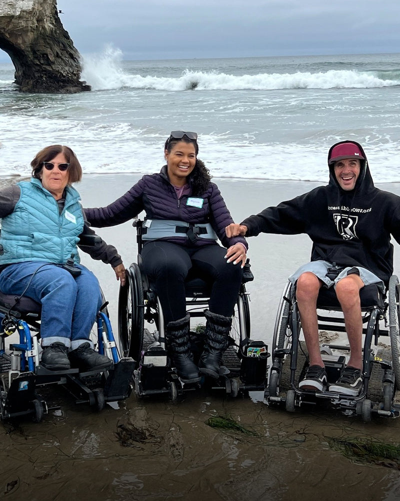 Three NorCal SCI members enjoying Natural Bridges Beach on their manual wheelchairs on top of a Freedom Trax on the sand.