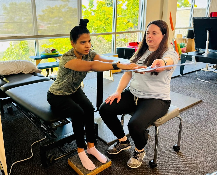 The Franklin Project recipient working with a physical therapist as they have their arms stretched forward while sitting on a bed