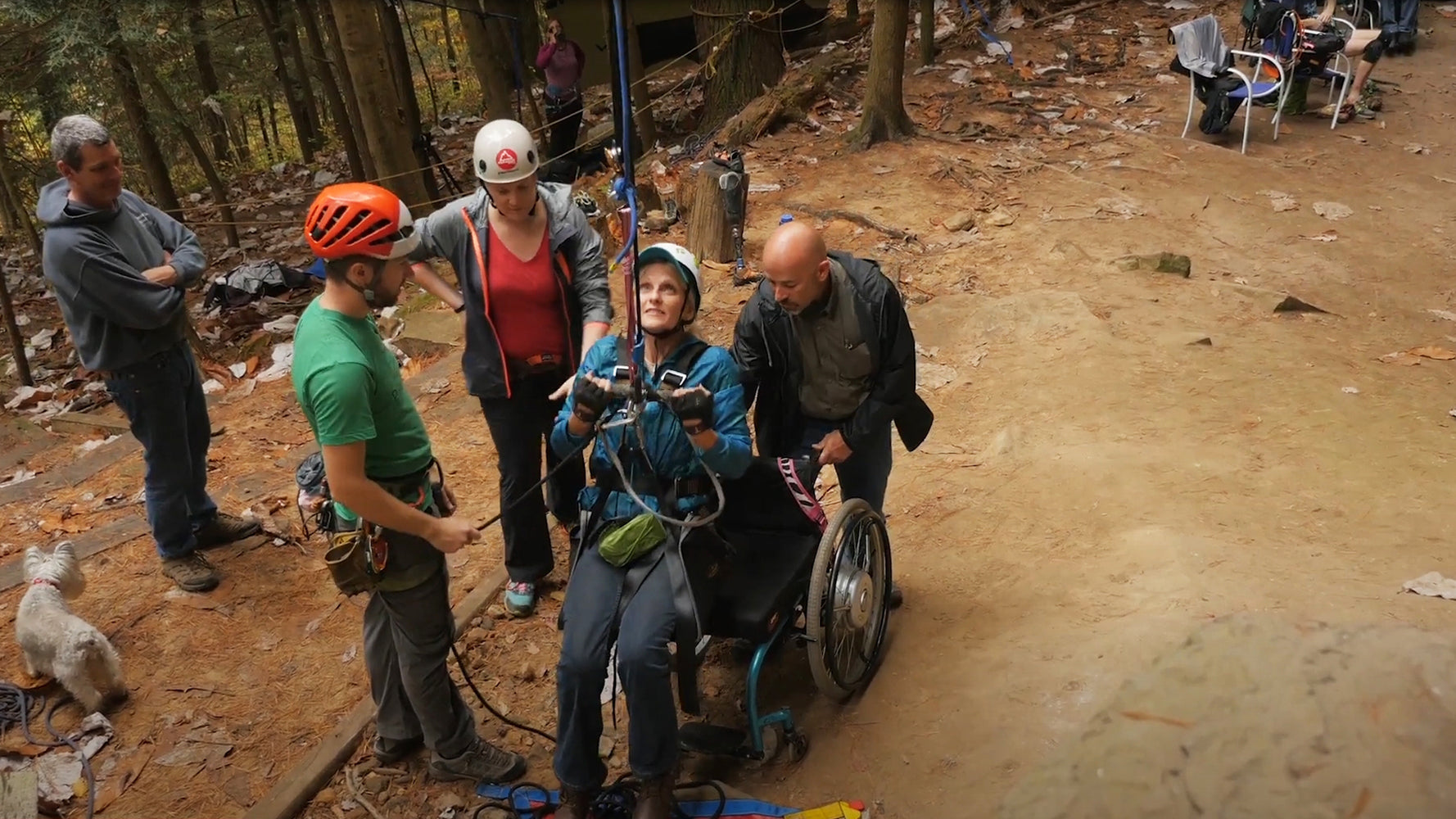 A climber hoisting themselves up from their wheelchair while their climbing group ensures they are safe.