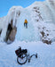 Person ice climbing a frozen waterfall with a wheelchair left on the snow below