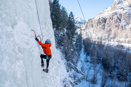 Person ice climbing a frozen waterfall with a snowy mountain landscape in the background