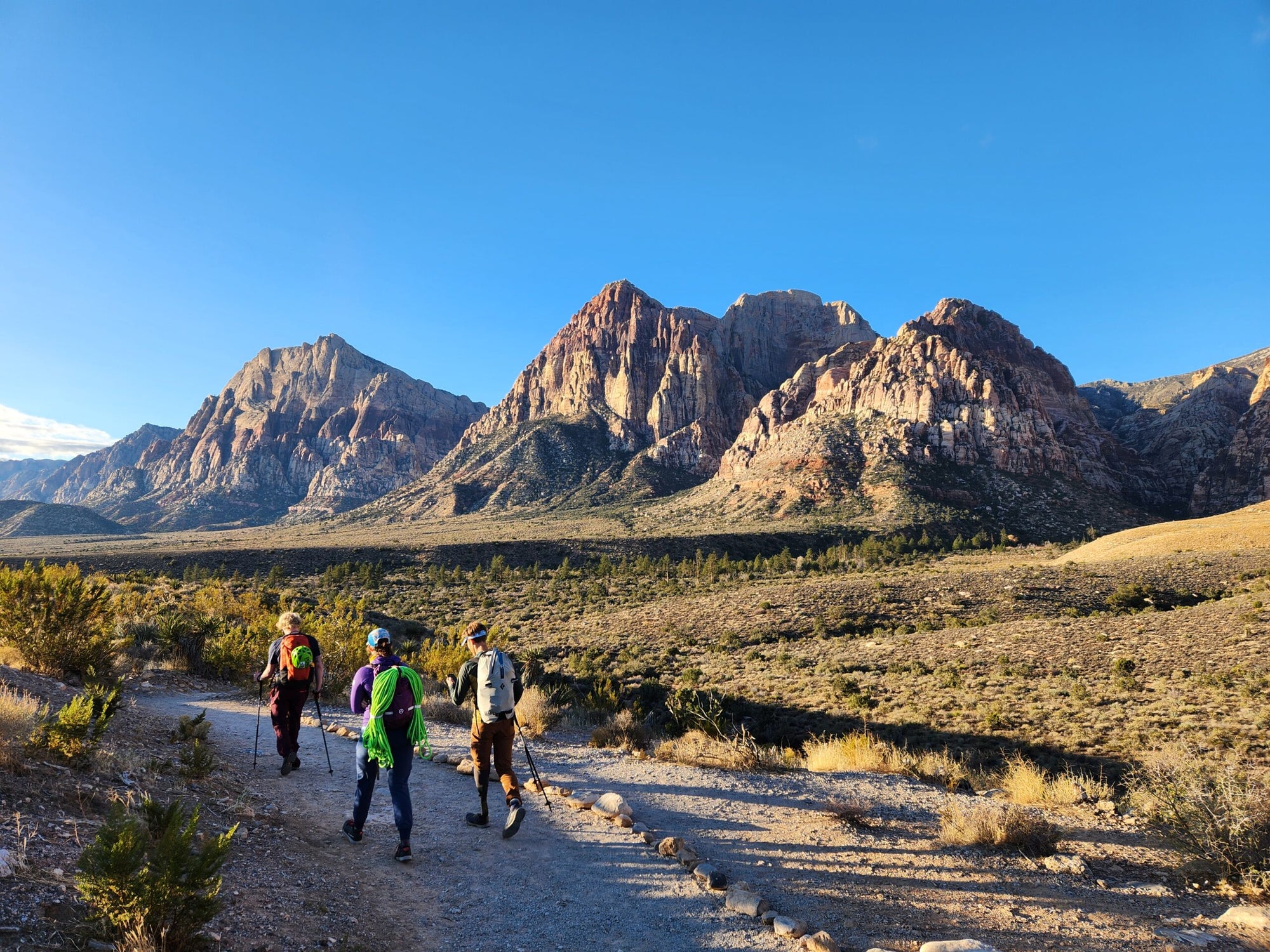 Three hikers on a trail with mountains in the background.