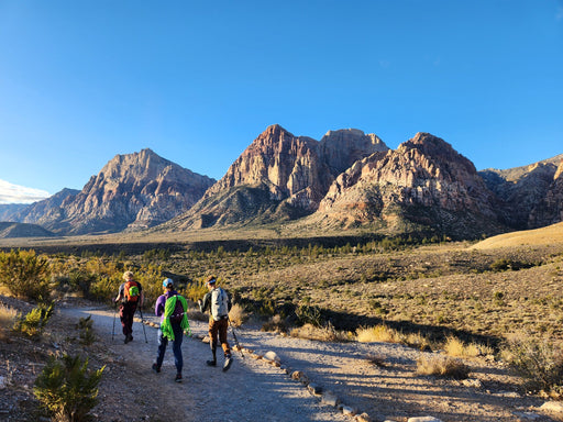 Three hikers on a trail with mountains in the background.