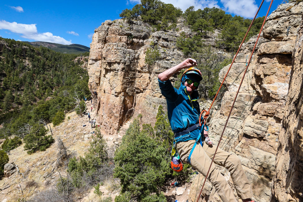Person rock climbing on a rocky cliff with a scenic background.