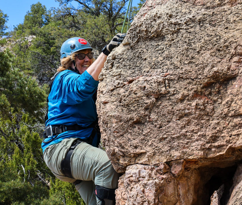 Person climbing a rock face with a helmet and sunglasses