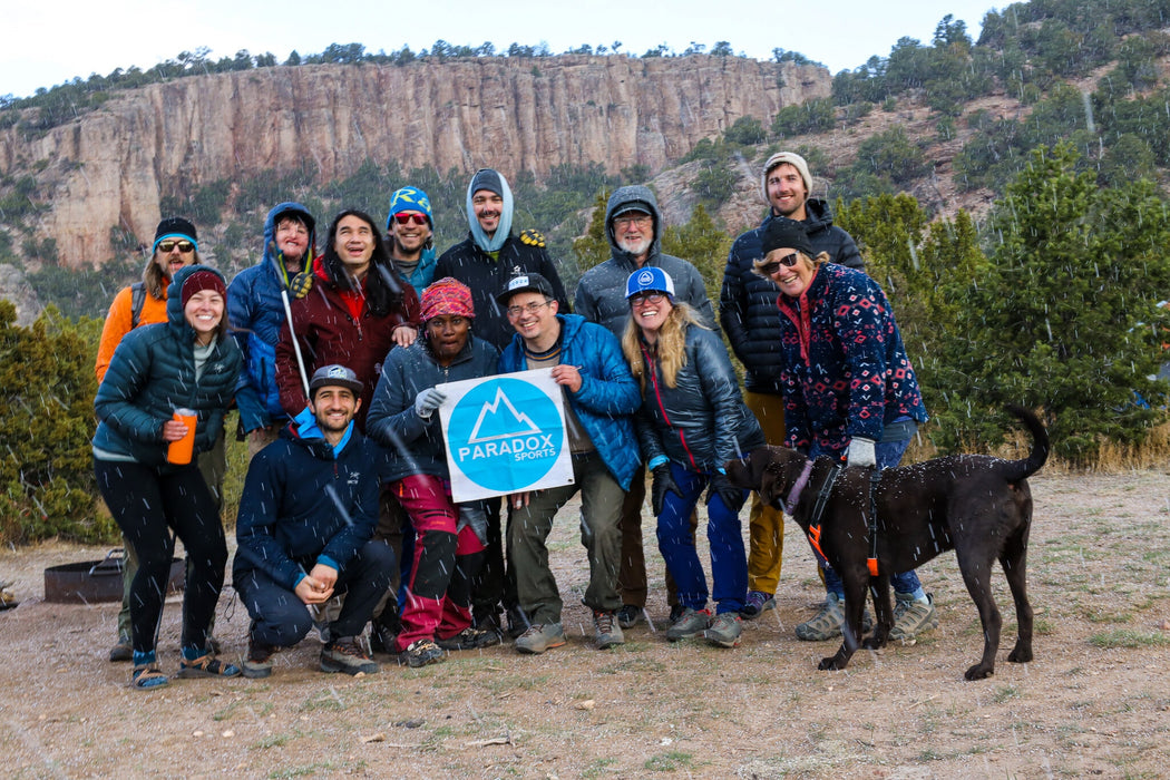 Group of people and a dog posing with a Paradox Sports Flag in a mountainous area