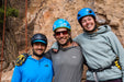 Three climbers posing together with rock climbing gear against a rocky background