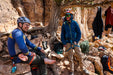 Two climbers taking a break on a rocky cliffside with climbing gear around them.